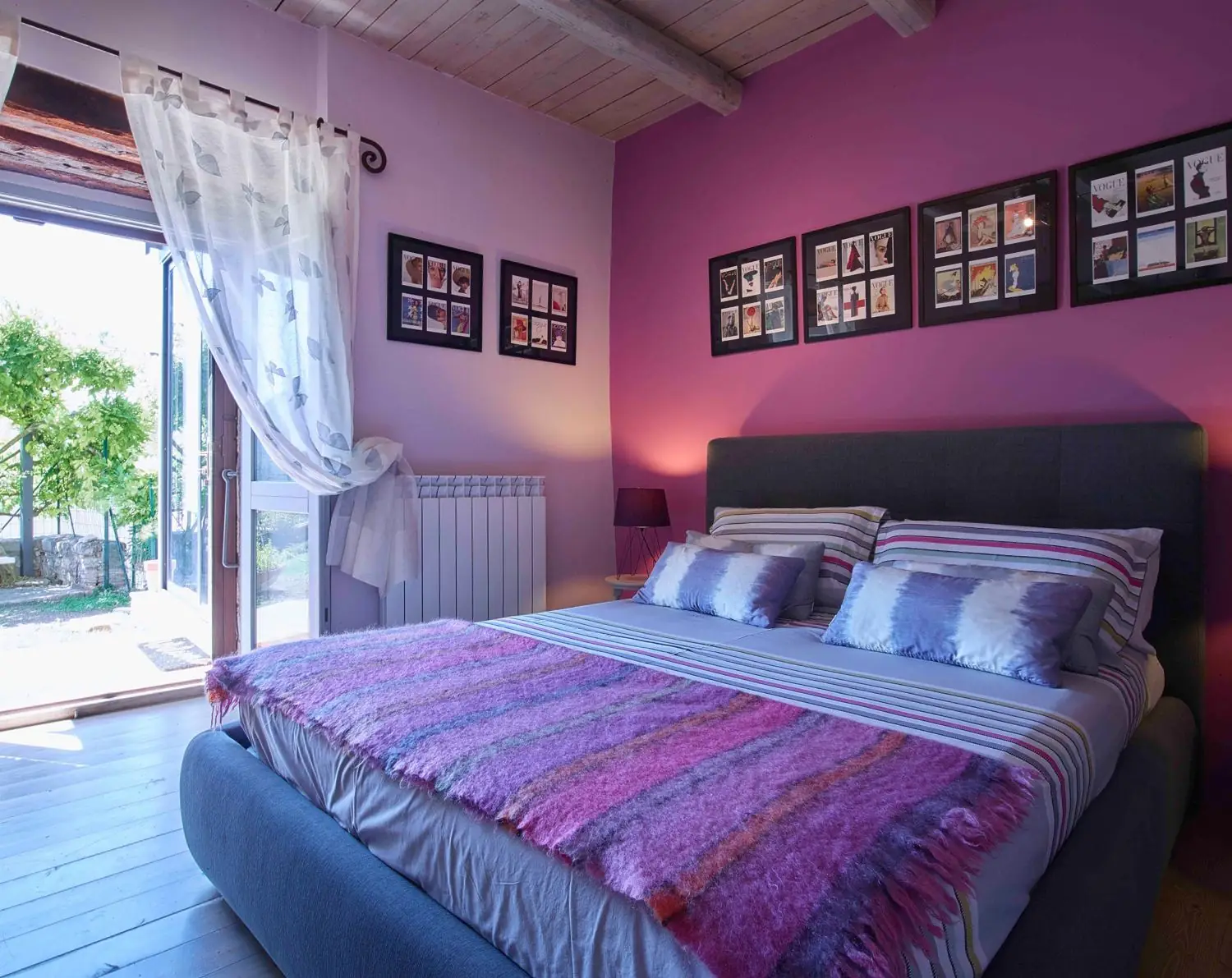 King bedroom with a pink wall and doors open to the garden