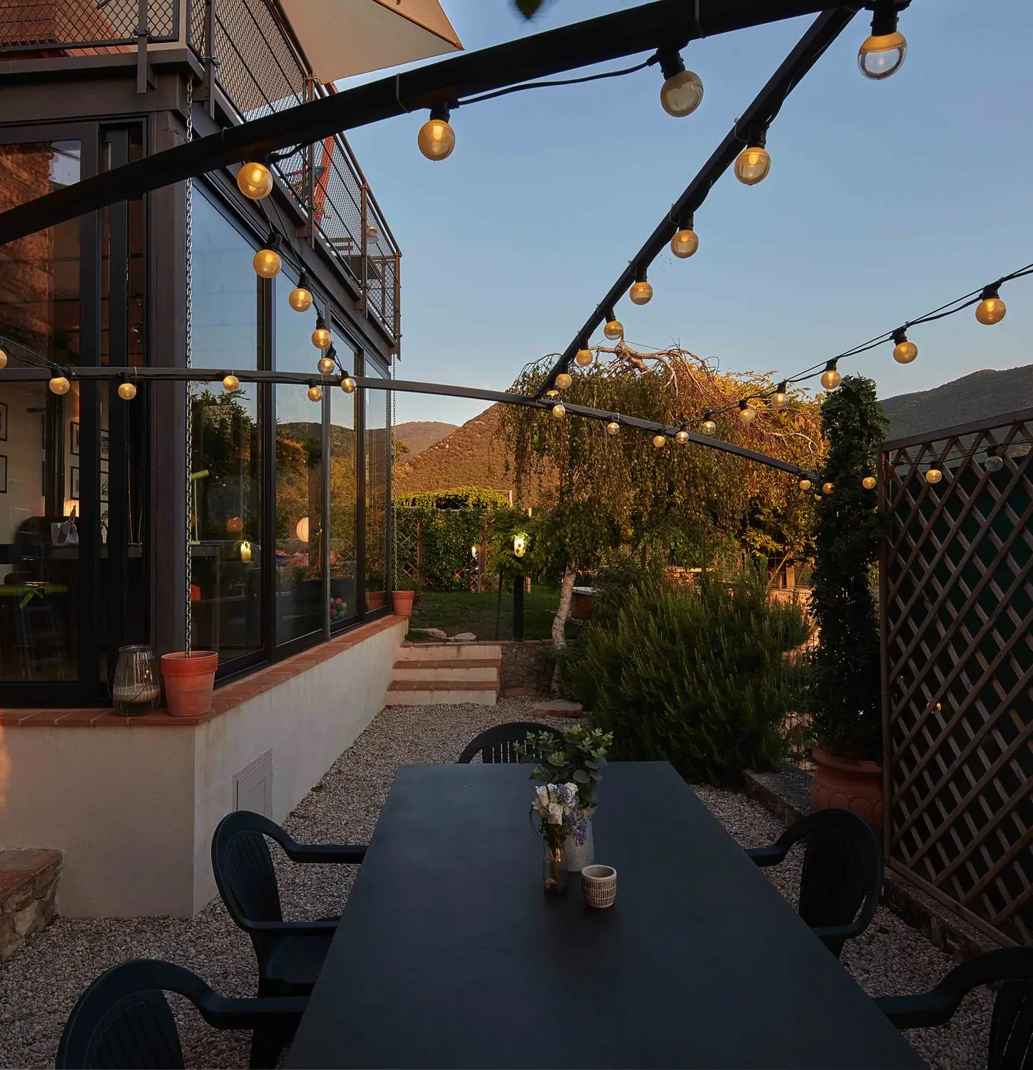 Garden dining table at dusk with festoon lights and the hills behind