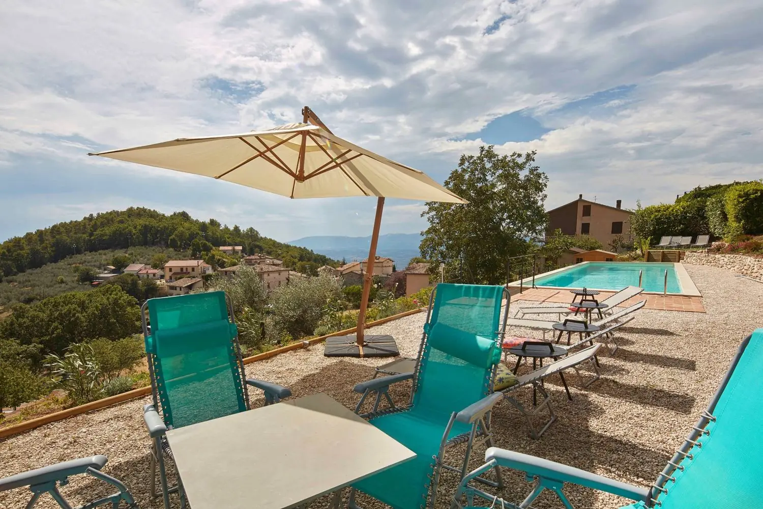 Loungers and a parasol beside the pool, with the village behind